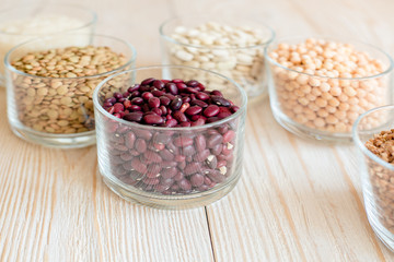 Grain and beans in glass bowls on white wooden background