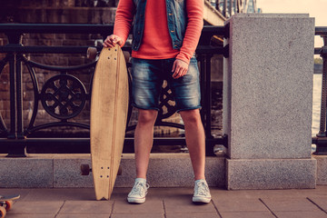 A man in jeans shorts holding longboard.