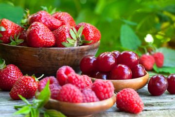 Fresh strawberries, raspberries and sour cherries in old wooden bowls