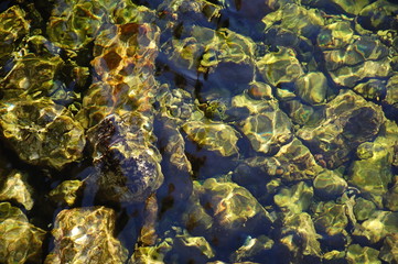 Seabed with pebble under water with solar patches of light. top view