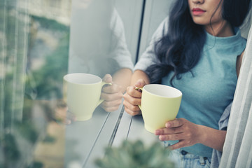 Cropped image of woman with cup of coffee standing at window