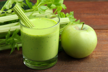 Fresh green celery juice in glass near green Apple on the brown wooden background