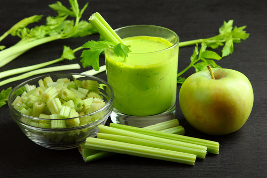 Fresh green celery in glass ball near the green Apple and glass of juice on a black wooden background