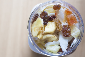 Plastic jar with mixed dried fruit over wooden surface