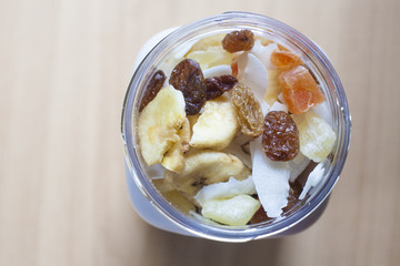 Plastic jar with mixed dried fruit over wooden surface