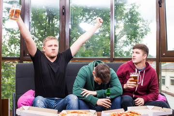 Young friends cheering and drinking alcohol while watching soccer match at home