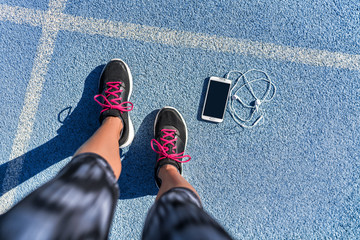 Running shoes girl feet selfie on blue track lane getting ready to run with smartphone and earbuds...