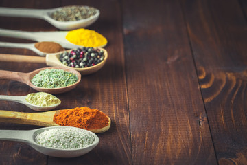 Beautiful colorful spices in wooden spoons on an old wooden brown table. Free space for your text