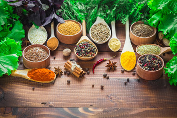 Beautiful colorful spices in wooden spoons and bowls with lettuce, dill and Basil on an old wooden brown table. Free space for your text