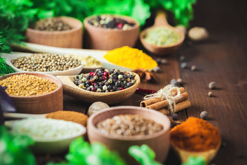 Beautiful colorful spices in wooden spoons and bowls with lettuce, dill and Basil on an old wooden brown table. Free space for your text
