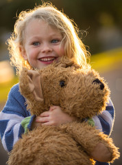 cute smiling child hugging a large teddy bear backlit by the sun