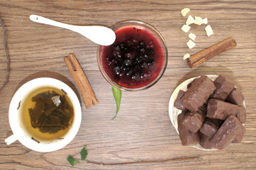 Composition with a Cup of tea, chocolates and a vase with currant jam on wooden background, top...