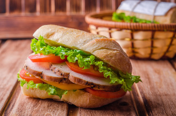 Homemade sandwich with fresh tomatoes and chicken breast in basket on wooden background. Selective focus. Picnic concept
