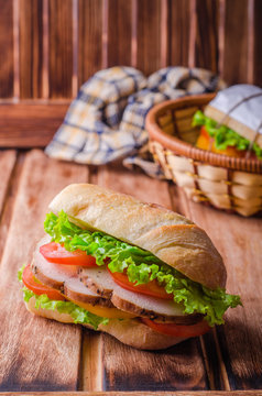 Homemade sandwich with fresh tomatoes and chicken breast in basket on wooden background. Selective focus. Picnic concept