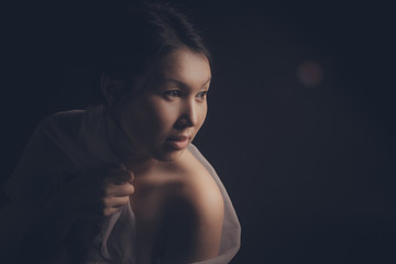 Woman on a black background, in the shadows, in a white transparent fabric. The natural beauty of the body and skin