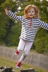 Jumping High. A  young girl attempts to spring off an old fallen tree trunk, to jump high in the air. She is being quite brave as she is scared she will hurt herself.