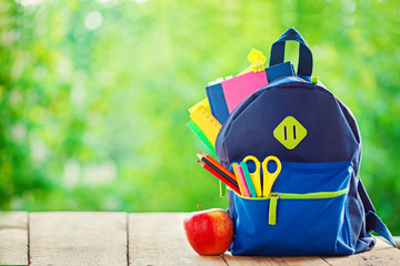 Full School backpack with apple on wooden and nature background.