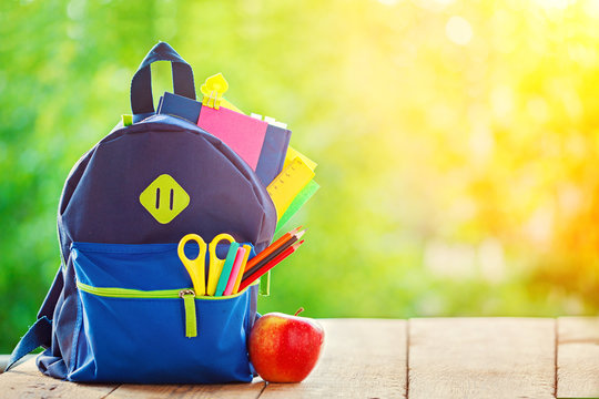 Full School backpack with apple on wooden and nature background.