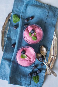 Two glasses with mixed berry mousse served with melissa leaves and blueberries. Selective focus.