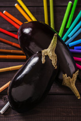 Fresh eggplant on a background of rainbow markers on dark wooden substrate 