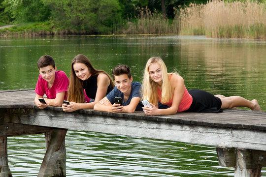 Gruppe Jugendliche liegen mit Smartphone draußen am See