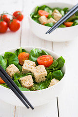 Vegan tofu salad with tomatoes and lamb's lettuce in bowl on white wood
