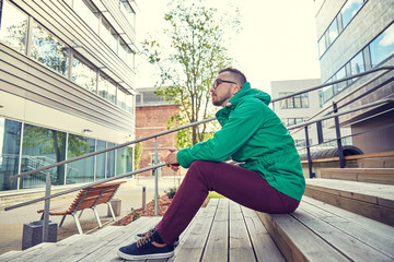 happy young hipster man sitting on stairs in city