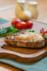 Juicy grilled pork chop (neck cut) on cutting board.