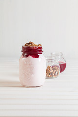 Homemade yogurt with jam and walnuts in a jar on a white wooden