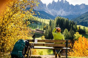 Tourist resting on the wooden bench and admiring the view of the mountains in the Dolomite, Alps