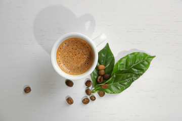 Cup of coffee with beans and leaves on light background