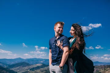 Fotobehang beautiful couple tender girl in a green dress and a guy in a bles shirt against the sky in a mountainous place © nataliakabliuk
