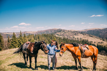 portrait of a cute couple with a horse in a mountains with blues sky. Couple walk and kiss near two horses.