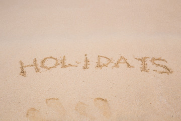 Word Holidays handwritten on sandy beach of tropical island