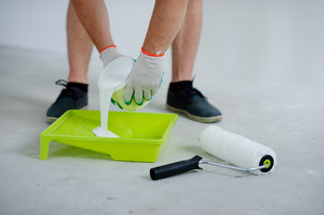 The person pours white paint in a tray.