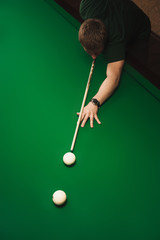 The guy plays billiards and aim the ball in the hole. Focus on center of photo. View from above. Empty space for text.