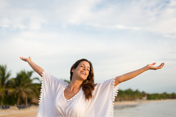 Blissful woman at tropical beach enjoying relax, freedom and vacation.  Brunette female raising arms to the sky. Summer happiness and leisure.