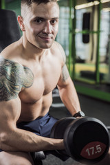 Fototapeta na wymiar young male bodybuilder with tattoos with dumbbells in hand in the gym