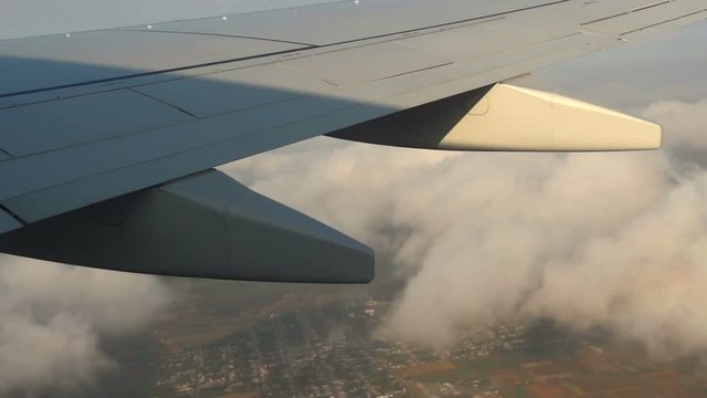 Airplane flying over clouds and village. Filmed from  commercial jet airplane window.