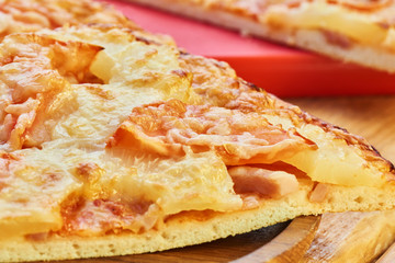 A slice of pizza with toppings of pineapple on a wooden plate