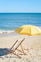 Yellow umbrella and wooden chair on Atlantic sandy beach