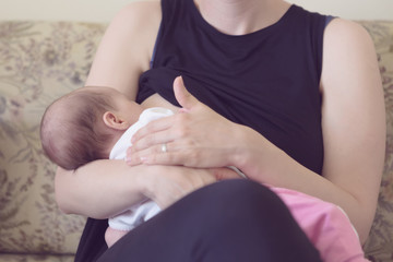 Obraz na płótnie Canvas Mother breastfeeding her newborn baby girl, sitting on a sofa, i