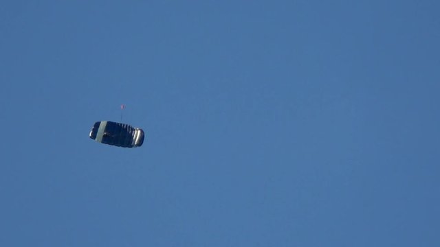 Skydiver moving down fast stunt moves like spiral and making turning loop beautiful blue sky background summer evening blue and white striped parachute man moving down quickly sky diving having fun 4k
