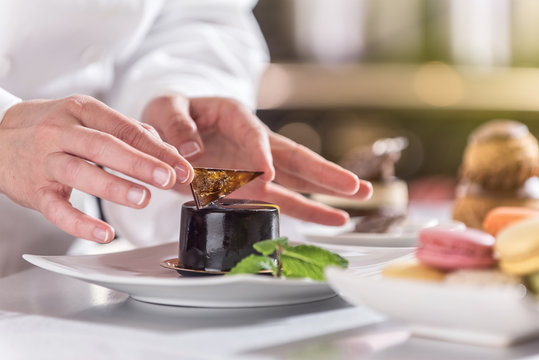 closeup on hands of a pastry chef depositing a chocolate leaf