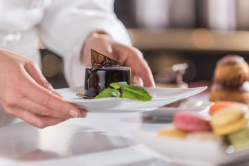 Obraz na płótnie Canvas closeup on hands of a pastry chef depositing a chocolate leaf