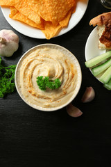 Ceramic bowl of tasty hummus with chips and parsley on table