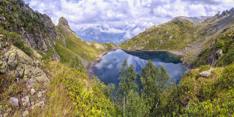 Fototapeta na wymiar panorama landscape with clear lake in the mountains, huge rocks and Alpika and reflection of white clouds in Abkhazia in the Caucasus.