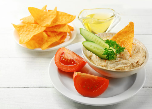 Ceramic bowl of tasty hummus with chips, oil and vegetables on table