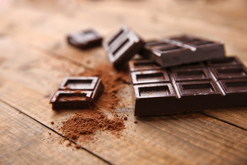 Dark chocolate with cocoa powder on wooden table