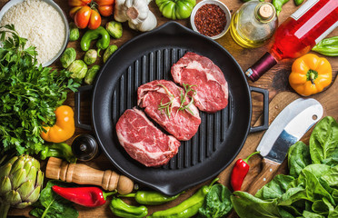 Fototapeta na wymiar Ingredients for cooking healthy meat dinner. Raw uncooked beef steaks with vegetables, rice, herbs, spices and wine bottle over rustic wooden background,